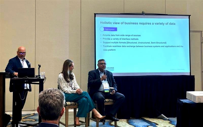 A panel discussion on data-driven business strategies, featuring a presentation slide and three speakers sharing insights with an engaged audience.