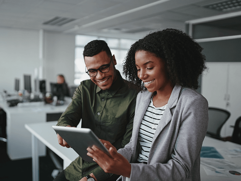 Smiling-young-african-american-professional-businessman-and-businesswoman-together-working-online-with-a-digital-tablet-in-office